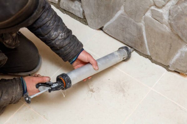 A man is working on a wall, applying caulk to the edge of a tile. Concept of diligence and attention to detail, as the man carefully applies the caulk to ensure a clean and professional finish