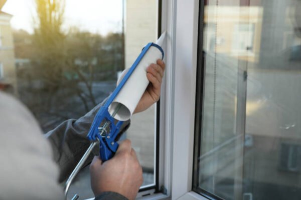 Construction worker sealing window with caulk indoors, closeup